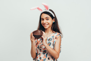 Wall Mural - Sweet little girl wearing bunny ears eating chocolate Easter egg. Easter in Brazil