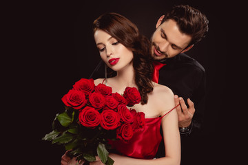 Wall Mural - Elegant man taking off dress from girlfriend with red roses isolated on black