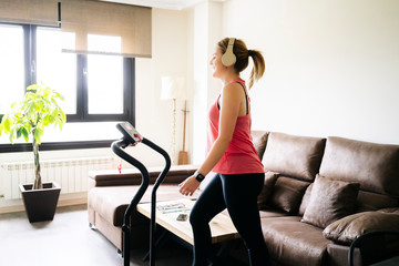 Beautiful caucasian blonde woman exercises on a treadmill in her living room