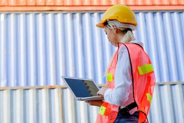 The back of technician woman work with laptop and stand in front of cargo containers with day light.