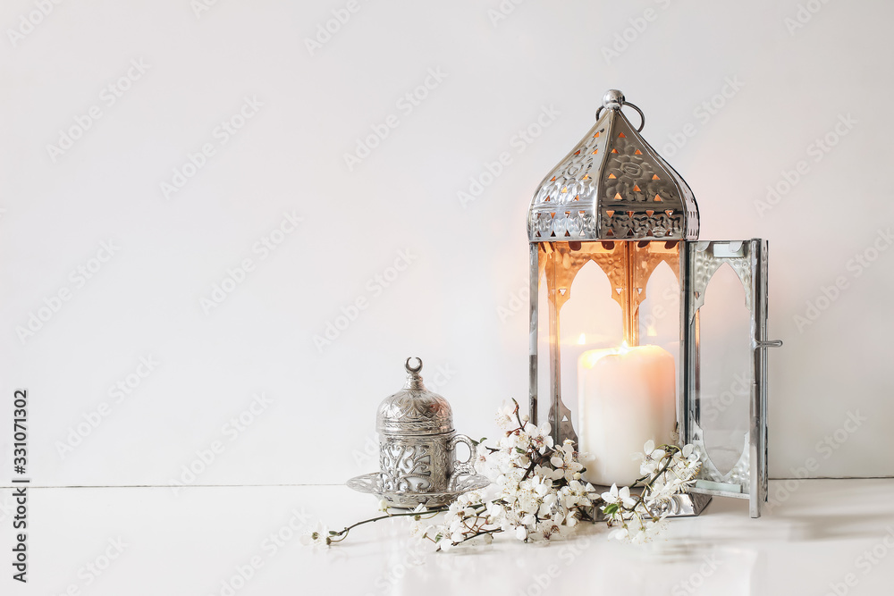 Silver decorative cup of tea, white flowers, prunus tree blossoms and glowing Moroccan lantern on table background. Iftar dinner. Ramadan Kareem greeting card, invitation. Eid ul Fitr muslim holiday. - obrazy, fototapety, plakaty 