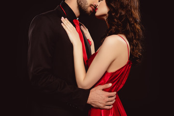 cropped view of elegant man in formal wear kissing and hugging girlfriend in red dress isolated on b