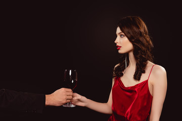 Wall Mural - Side view of man giving glass of red wine to elegant girl isolated on black