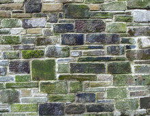 An Old Grey Stone Wall Made Of Large Irregular Blocks Covered In Patches Of Moss