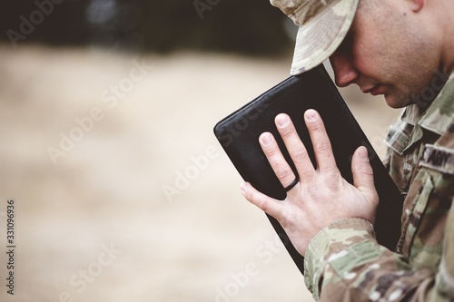 Fotografía Shallow focus shot of a young soldier praying while holding the bible