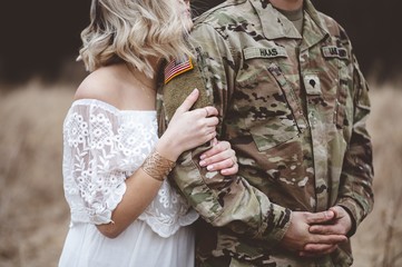 american soldier with his loving wife standing in a dry grassy field