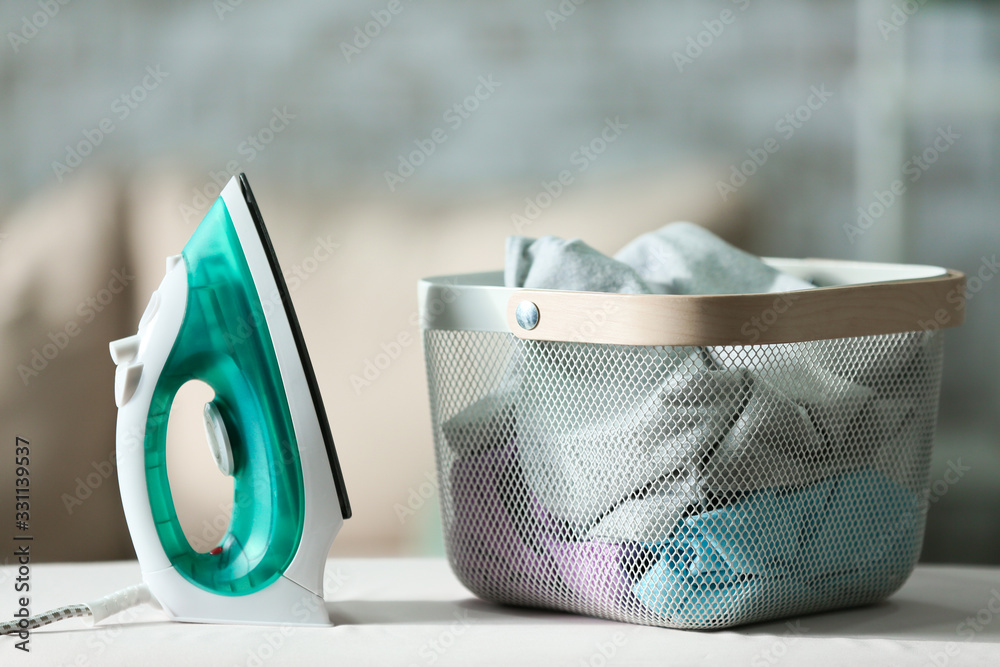 Electric iron and clothes in basket on board at home