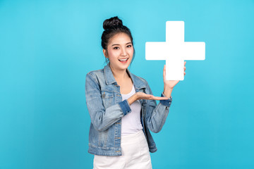 Wall Mural - Happiness asian woman smiling, showing plus or add sign and other hand open on blue background. Cute asia girl wearing casual jeans shirt and showing join sign for increse and more benefit concept