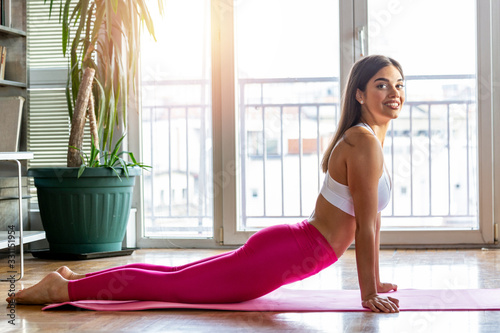 Photo of a beautiful female stretching on the floor sitting on a mat. Young beautifull woman stretching on the floor. Home training exercises, work out from home