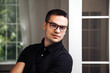 © Vadim - Adult man in a black shirt in eyeglasses with black rim. Male poses near window. Close-up
