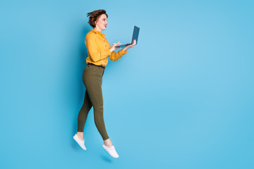 Poster - Full size profile photo of beautiful lady jumping high up holding browsing notebook workaholic wear yellow shirt green pants shoes isolated bright blue color background