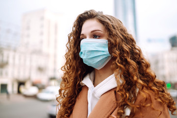 Girl in protective sterile medical mask on her face on the street. Woman, wear face mask, protect from infection of virus, pandemic, outbreak and epidemic of disease in  quarantine city. Corona virus.