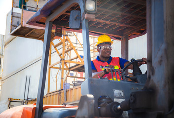 Happy worker man in hardhat and safety vest driving container stackers for control loading containers box from cargo