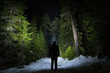 Figure on forest path at night with headlamp illuminating the trees and path