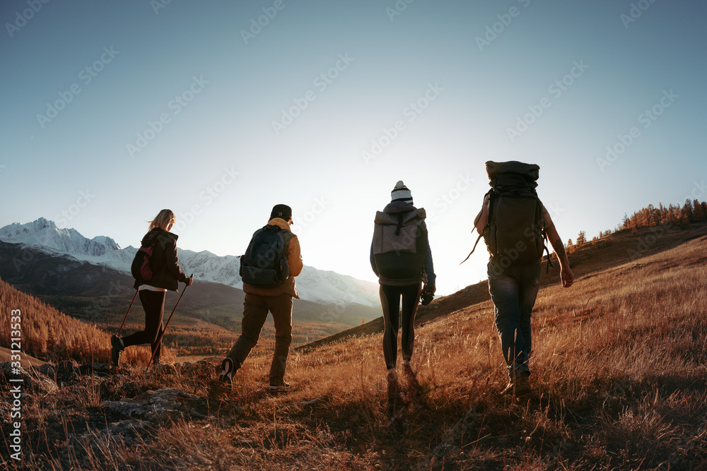 Four hikers or backpackers walks in sunset mountains - obrazy, fototapety, plakaty 