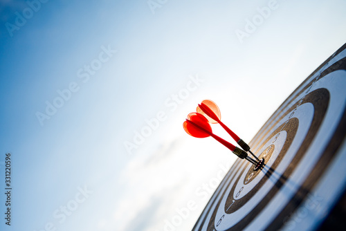 Fotomural Close up shot red darts arrows in the target center on dark blue sky background