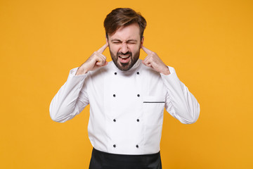 Wall Mural - Irritated young bearded male chef cook or baker man in white uniform shirt isolated on yellow background. Cooking food concept. Mock up copy space. Keeping eyes closed, covering ears with fingers.