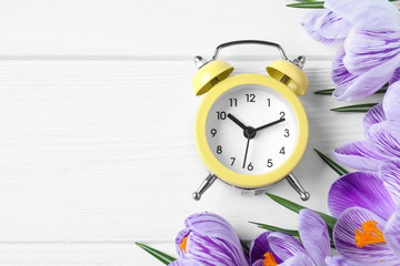 Poster - Yellow alarm clock, spring flowers and space for text on white wooden table, flat lay. Time change