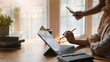 Cropped image of creative woman holding a stylus pen for drawing on computer tablet with keyboard case while sitting at the wooden working table next to her friend in comfortable living room.
