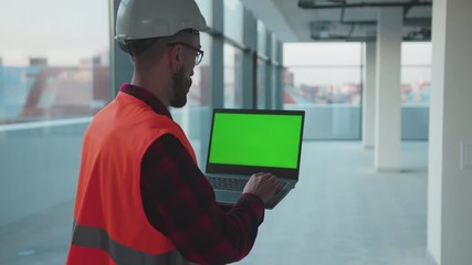 Wall Mural - Inside in building man engineer stand using laptop computer with green screen worker project occupation builder technology mock-up professional male safety device computer slow motion