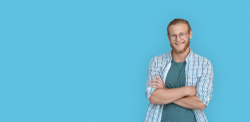 Smiling confident young bearded handsome man hipster wear shirt glasses looking at camera, millennial handsome casual guy student arms crossed isolated on blue studio background, portrait, copy space.