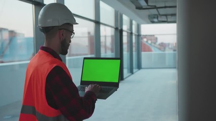 Wall Mural - Professional engineer man with helmet using laptop computer with green screen inside building worker project occupation builder technology mock-up professional male safety device computer slow motion