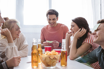 Wall Mural - cheerful man looking at sticky note while playing name game with happy friends