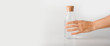 © Elena - A hand takes a glass bottle filled with clear water on a white background.