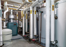 Boiler Room Of Residential, Strata Or Multilevel Building. 3 Hot Water Boiler Visible. Many Insulated Pipes With Yellow Arrows To Direction Of Water Flow.