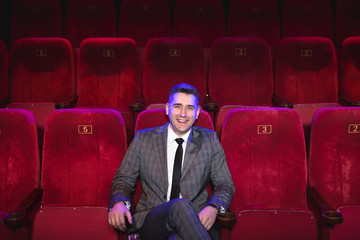 Portrait of a young handsome man alone in a movie theater in a business suit