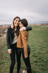 Two laughing girls hugging on field with city view