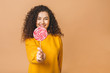 © denis_vermenko - Surprised curly girl eating lollipop. Beauty Model woman holding pink sweet colorful lollipop candy, isolated on beige background.