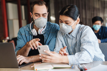 Sticker - Photo of young students in medical masks using cellphone while studying