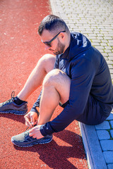 Man tying jogging shoes. A person running outdoors on a sunny day.Focus on a side view of two human hands reaching down to a athletic shoe. Young male runner getting ready to start.