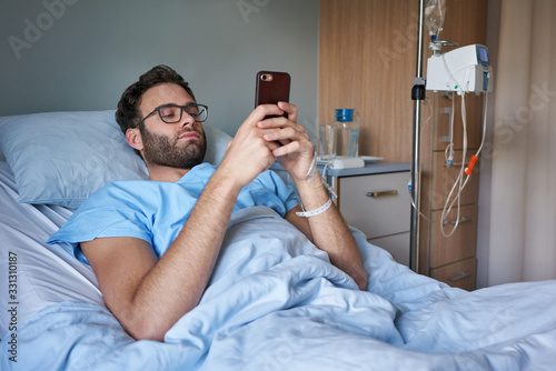 Young man lying in a hospital bed using his cellphone