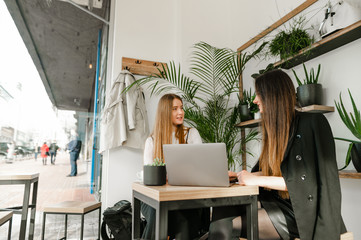 two young girls in formal wear sitting in a cozy cafe with a laptop and discussing business with smi