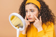 © denis_vermenko - Beauty portrait of an astonished shocked amazed attractive curly woman examining her face while holding a mirror isolated over beige background.