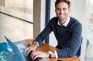 Wall Mural - Smiling young businessman working on a laptop at home