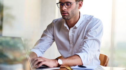 Wall Mural - Young businessman sitting at a table working on a laptop