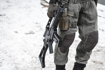 A military man with a machine gun down is walking along the road.