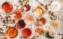 Various Shades Of Rose Wine. Flat-lay Of Rose Wine In Different Colors In Glasses And Spring Blossom Flowers Over Marble Background, Top View. Wine Shop, Bar, Tasting, Seasonal Wine List Concept