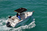 Open white sport fishing boat with canopy covered center console powered by a single outboard engine.