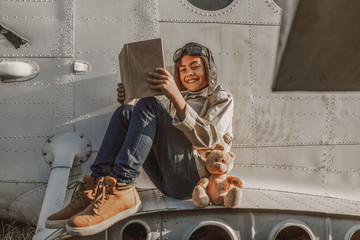 Happy cute child sitting near plane with book outdoors