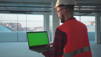 Wall Mural - Shot back man engineer using laptop computer with green screen inside building worker project occupation builder technology mock-up professional male safety device computer slow motion