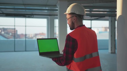 Man stand look around engineer using laptop computer with green screen inside building worker project occupation builder technology mock-up professional male safety device computer slow motion