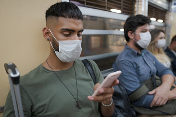 young man uses his cellphone inside the train car. traveler wears mask to prevent spread of coroviru