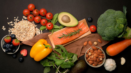 Top view of healthy food assortment with salmon, fruits, vegetable   and seeds on black table