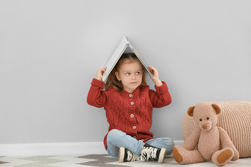 Poster - Cute little girl with book and toy near grey wall