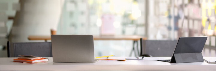 Cropped shot of portable workspace with laptop and tablet in glass wall office