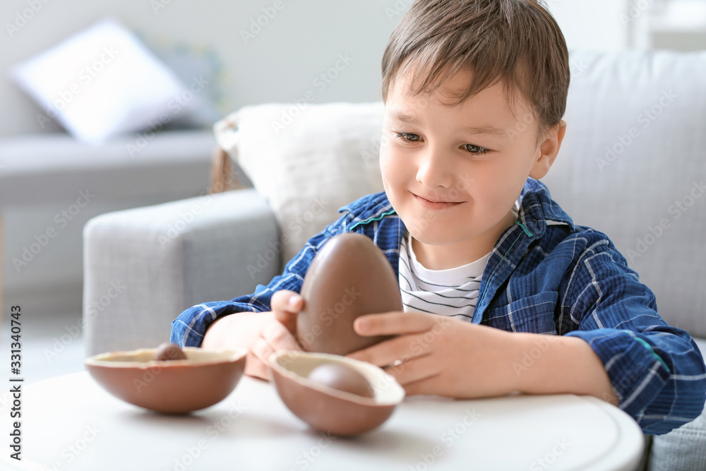 Cute little boy with sweet chocolate eggs at home